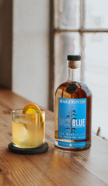 Bottle of Baby Blue Straight Corn Whisky with a glass of baby blue imposterita on table