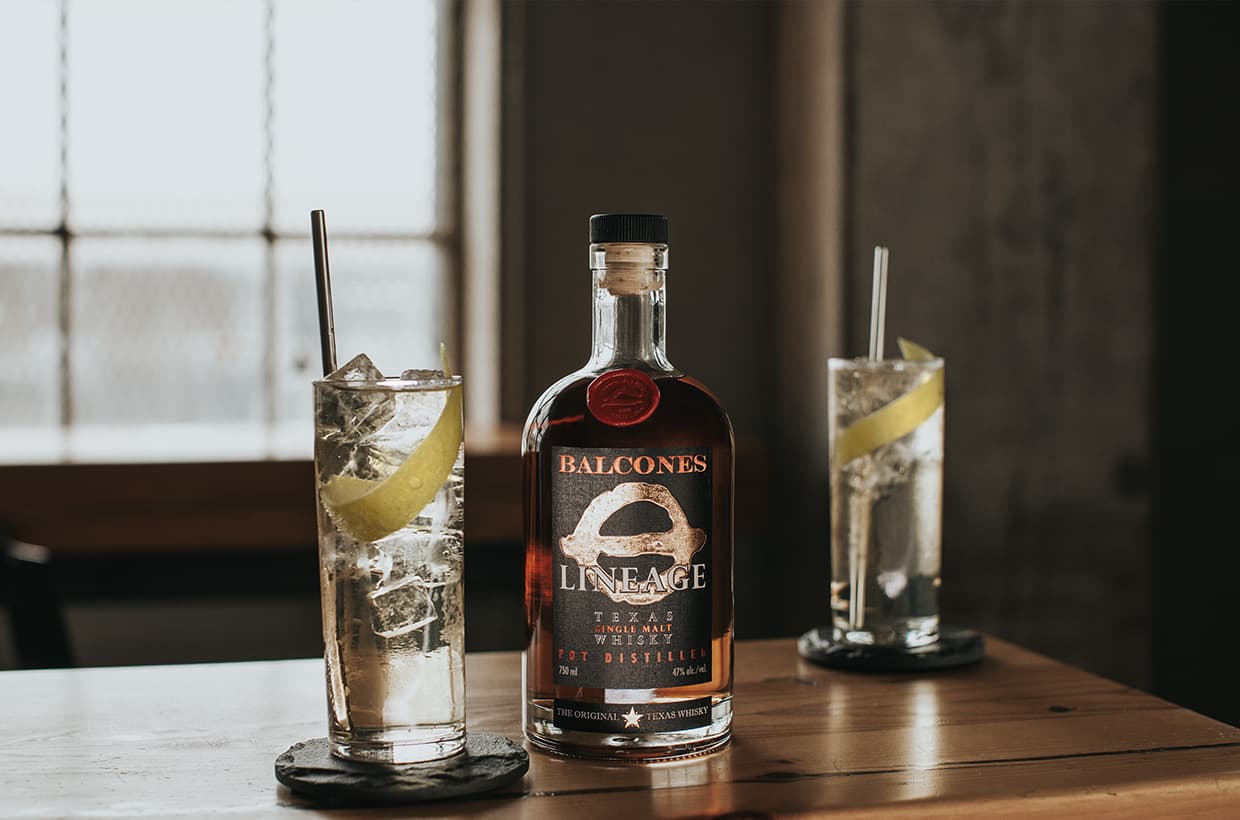Bottle of Lineage Texas Single Malt Whisky with two glasses of Highball cocktails on table