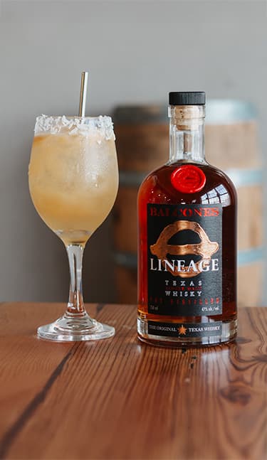 Bottle of Lineage Texas Single Malt Whisky with two glasses of Balcola cocktails on table