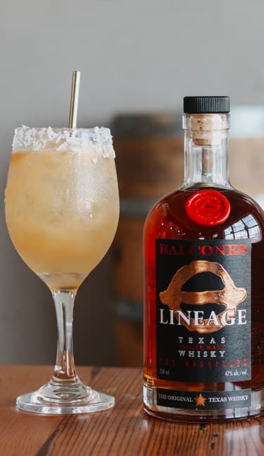 Bottle of Lineage Texas Single Malt Whisky with two glasses of Balcola cocktails on table