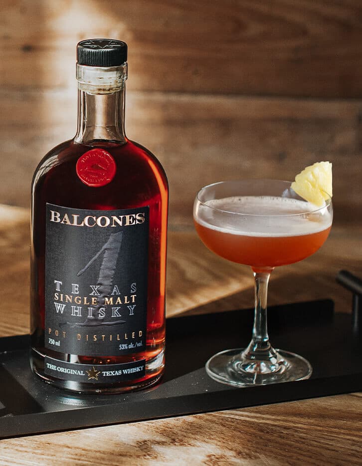 A bottle of Texas 1 Single Malt Whisky with next to a Halekulani cocktail.