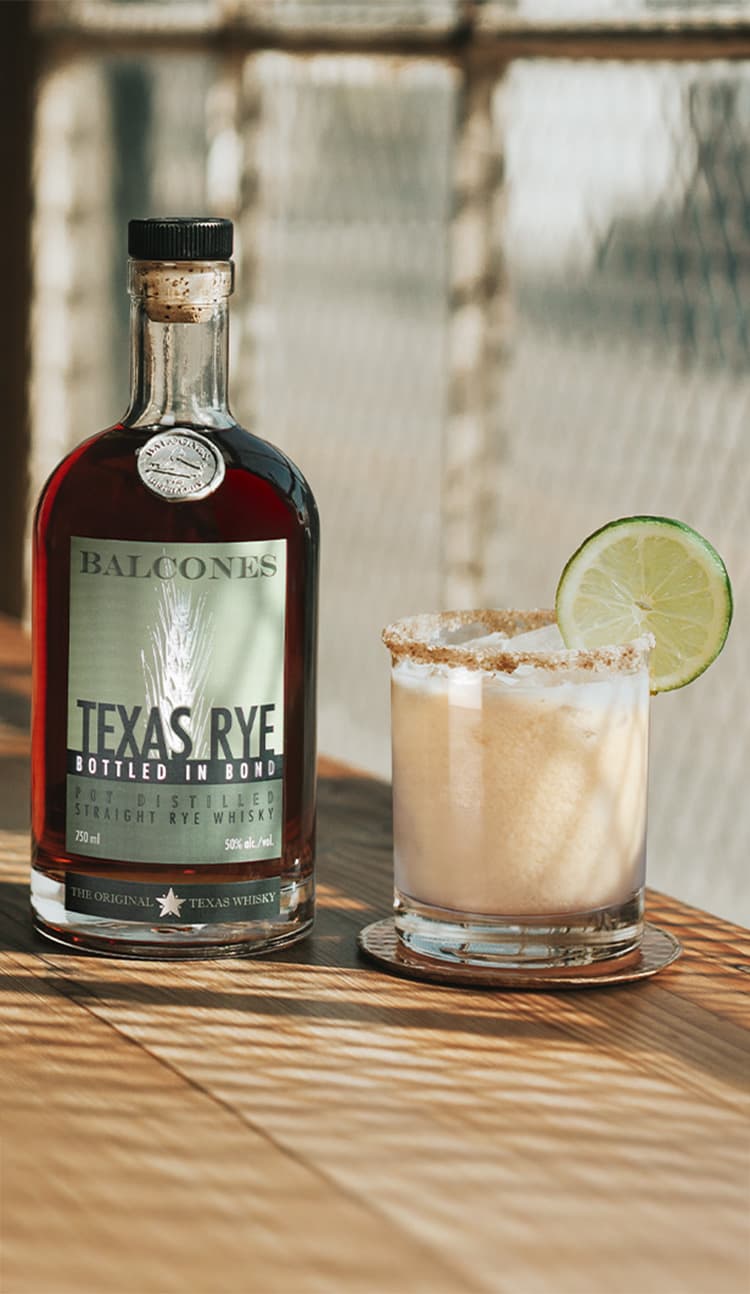 A bottle of Texas Rye Bottled in Bond next to a Key Lime Rye cocktail on a table.
