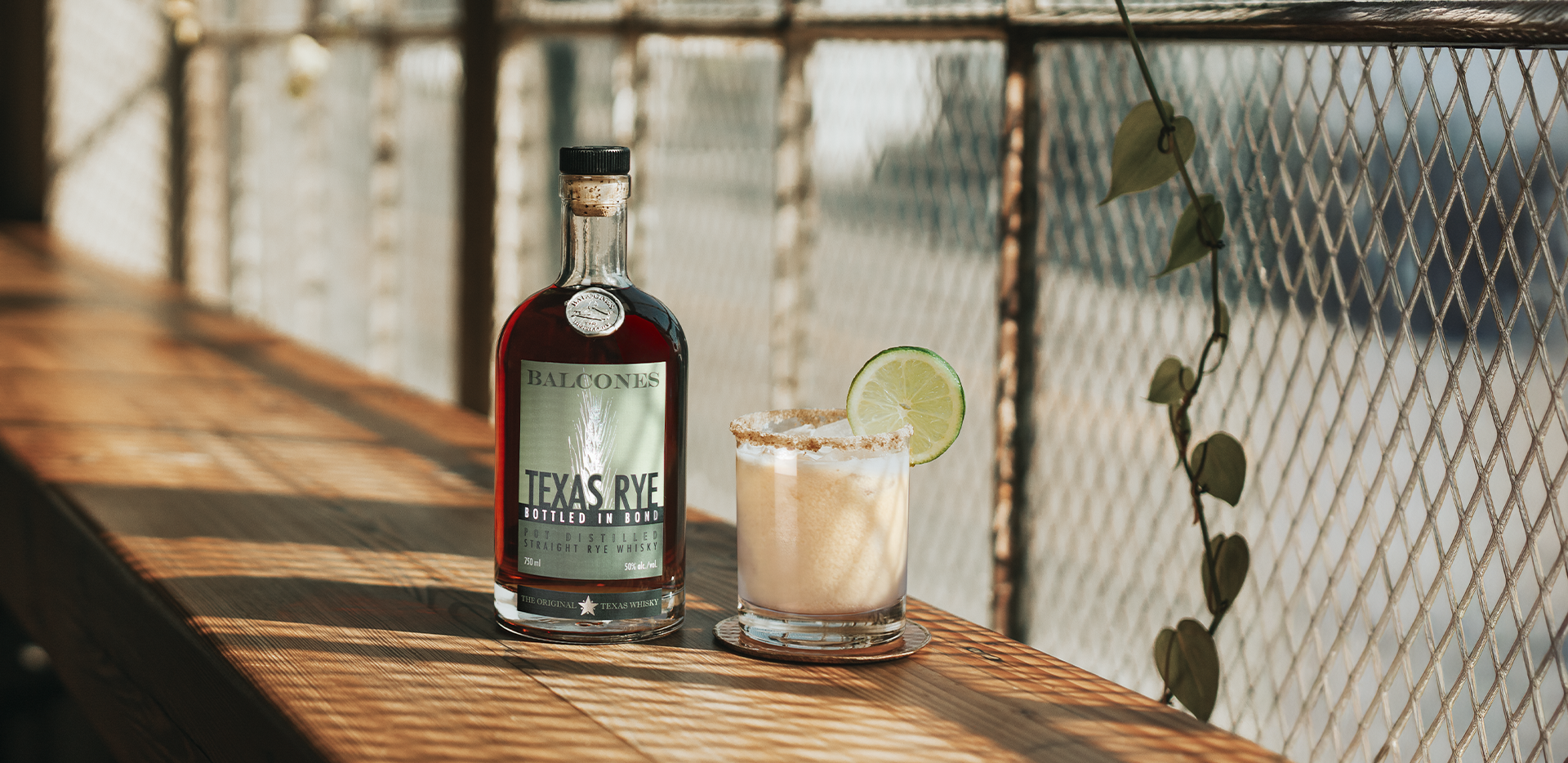A bottle of Texas Rye Bottled in Bond next to a Key Lime Rye cocktail on a table.