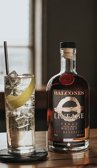 Bottle of Lineage Texas Single Malt Whisky with two glasses of Balcola cocktails on table