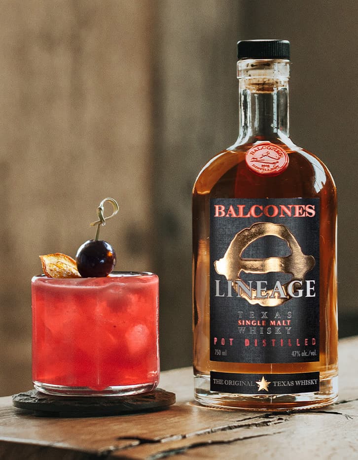 A bottle of Lineage Texas Single Malt Whisky with a Raspberry Fix cocktail on a table.
