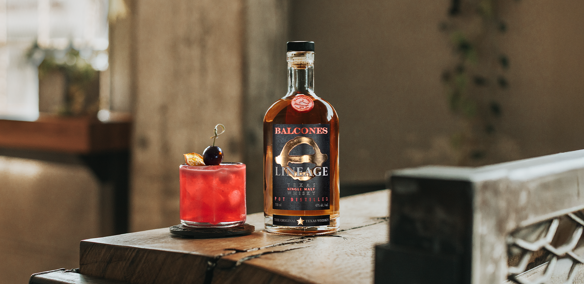 A bottle of Lineage Texas Single Malt Whisky with a Raspberry Fix cocktail on a table.