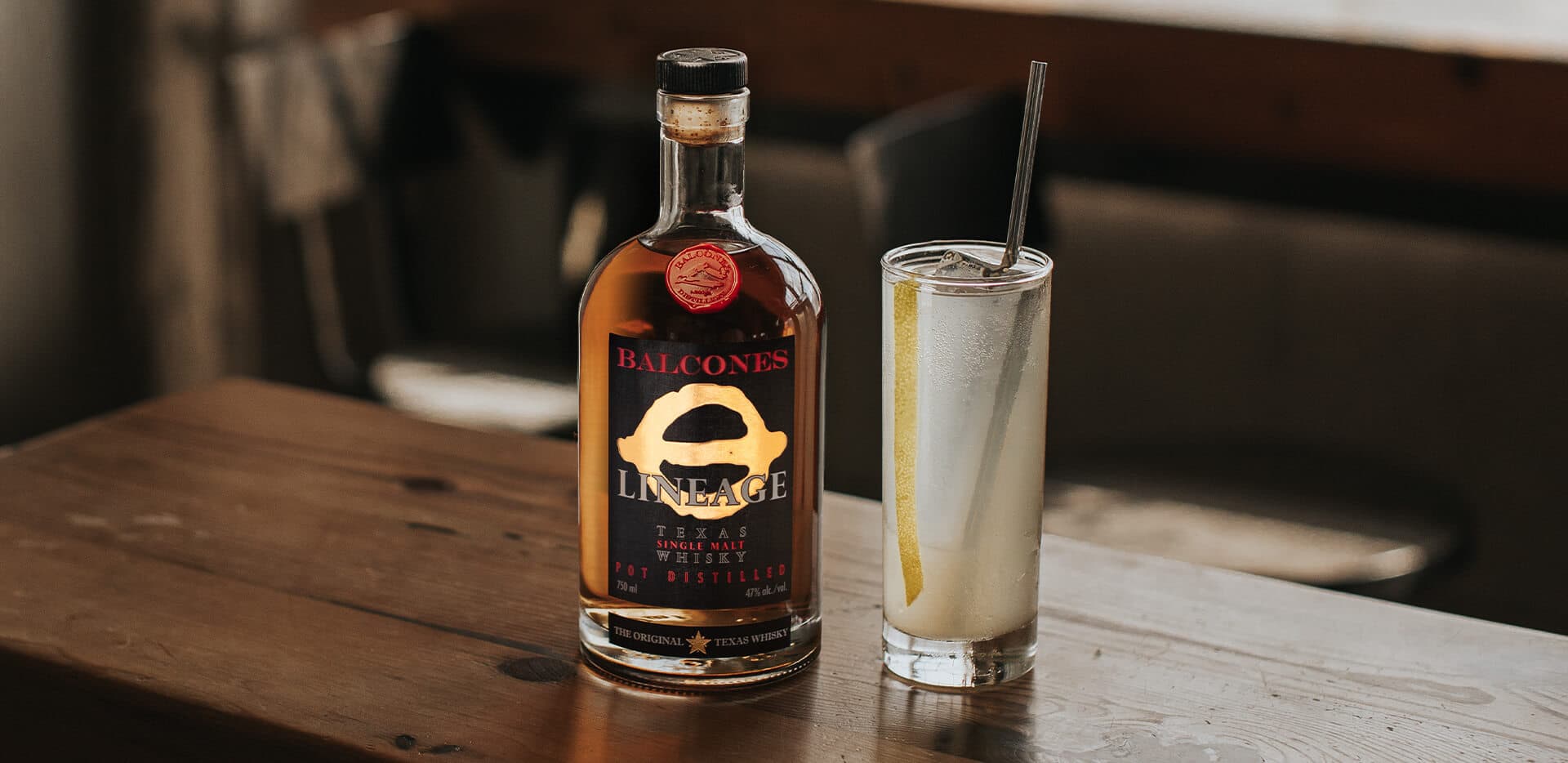 Bottle of Lineage Texas Single Malt Whisky with a glass of Texas Collins cocktail on a table.