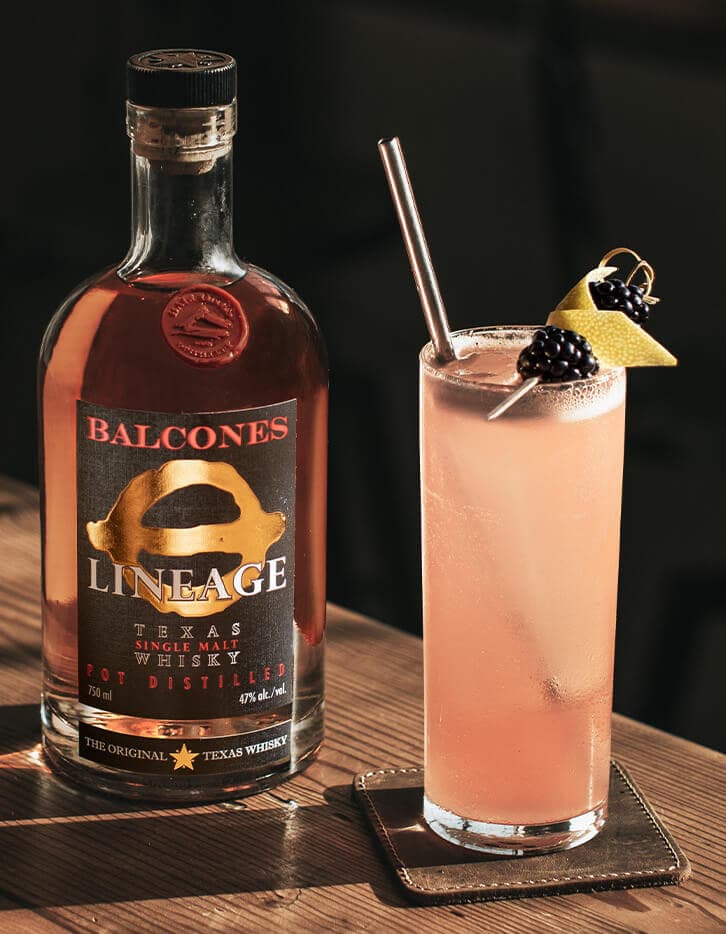 A bottle of Lineage Texas Single Malt Whisky with an Under the Elder Tree cocktail on a table.