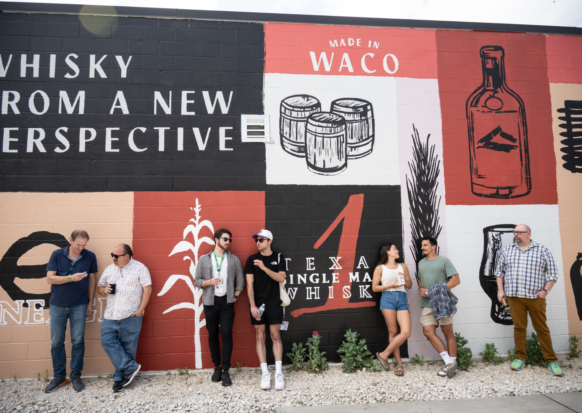 Group of people leaning against Balcones' mural