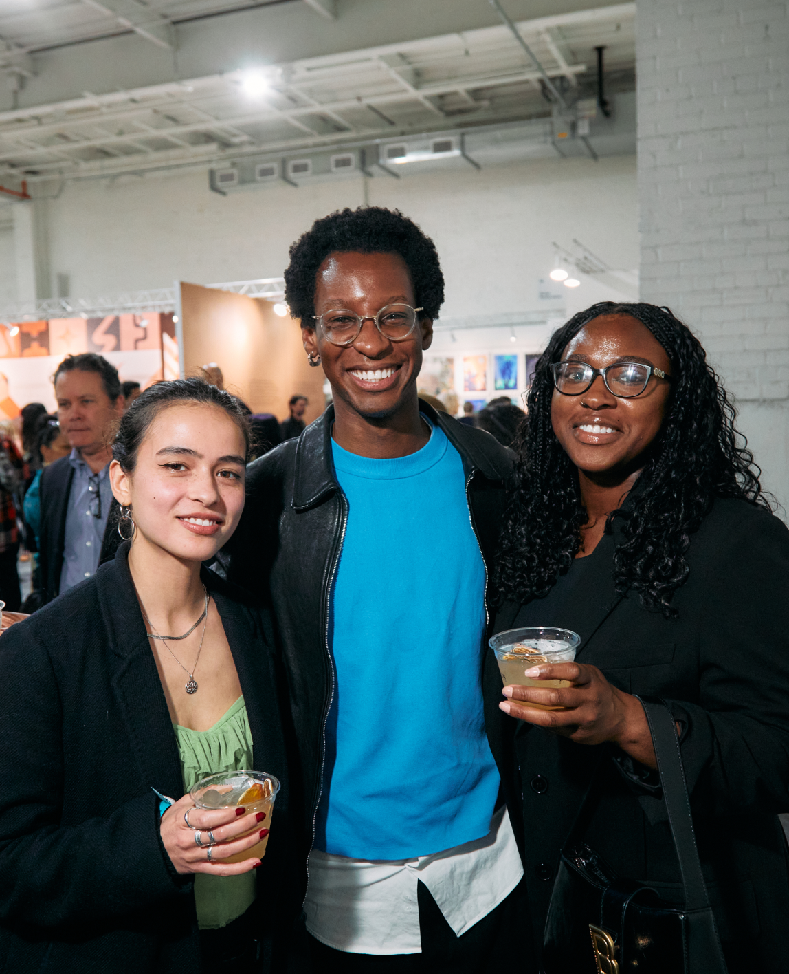 Three people smiling at camera inside event with cocktails
