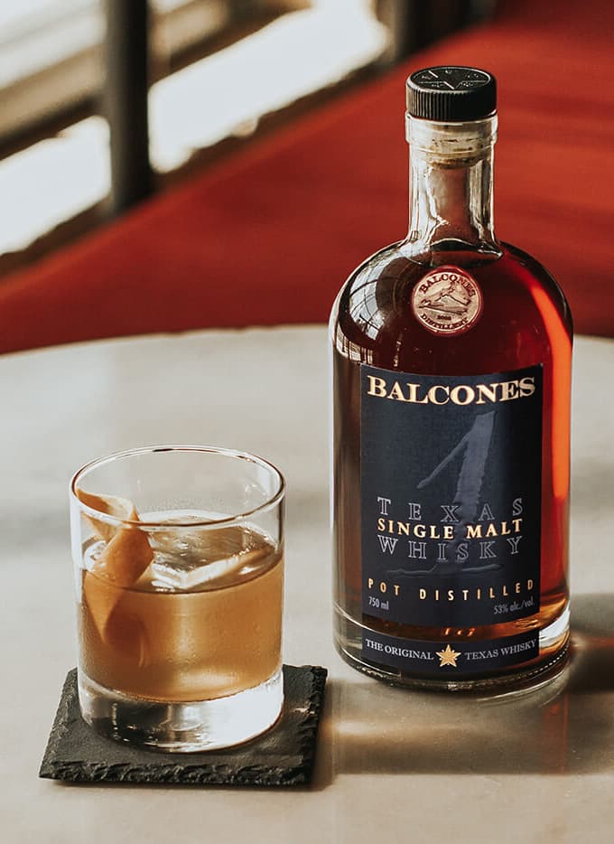 A bottle of Texas 1 Single Malt Whisky with a Texas 1 Old Fashioned cocktail on a table.