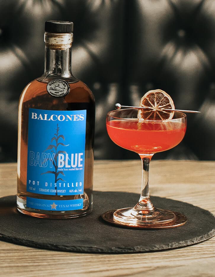 A bottle of Baby Blue Straight Corn Whisky with a glass of Texas Rose cocktail.