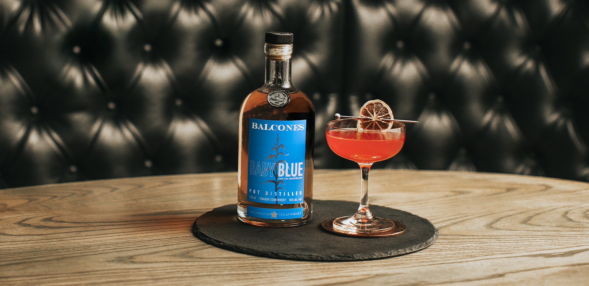 A bottle of Baby Blue Straight Corn Whisky with a glass of Texas Rose cocktail.