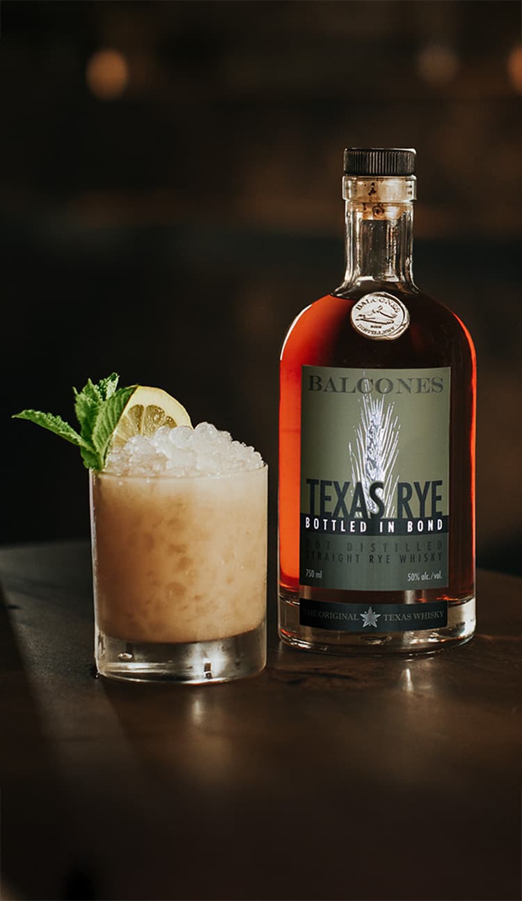 A bottle of Texas Rye Bottled in Bond next to a Texas Rye Tai cocktail on a table.