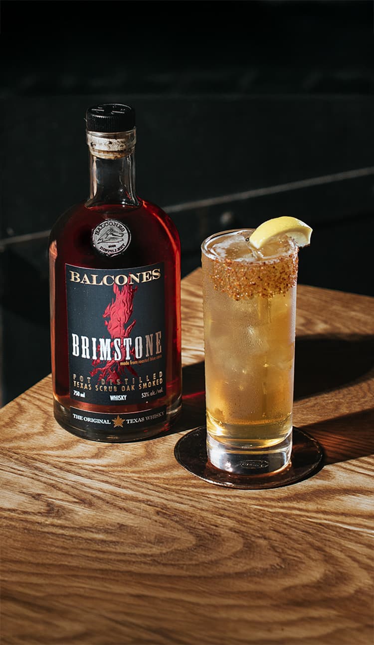 A bottle of Brimstone Smoked Whisky with a Texas Tonic cocktail on a table.