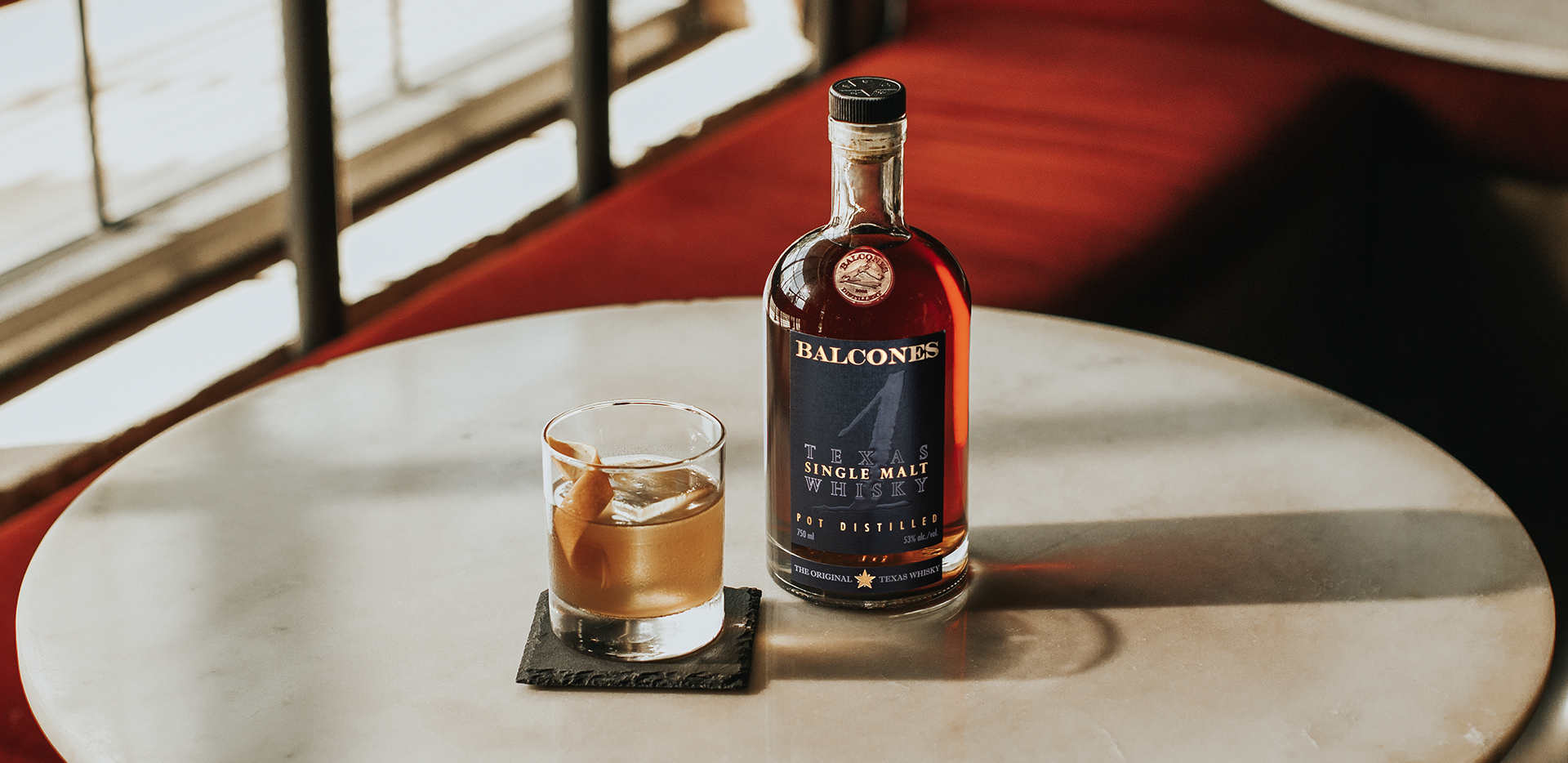 A bottle of Texas 1 Single Malt Whisky with a Texas 1 Old Fashioned cocktail on a table.