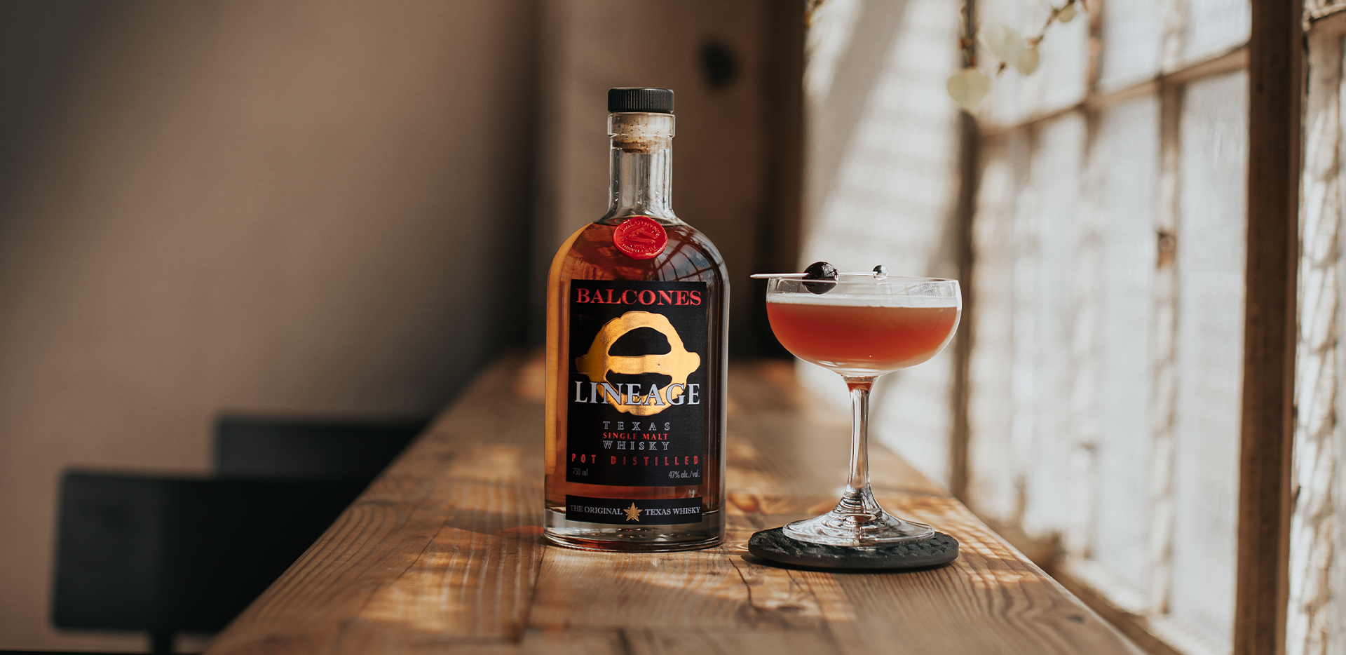 Bottle of Lineage Texas Single Malt Whisky next to Waco Sour cocktail in a martini glass.