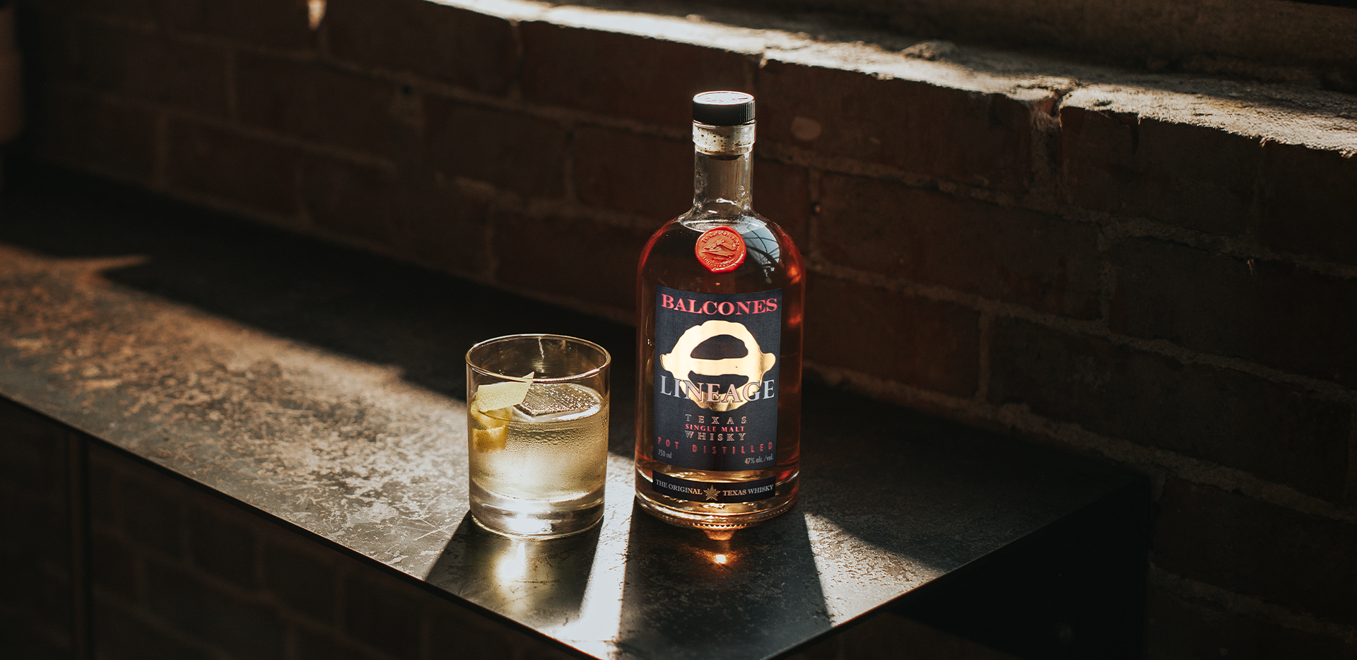 Bottle of Lineage Texas Single Malt Whisky with a glass of White Negroni cocktail on a table.